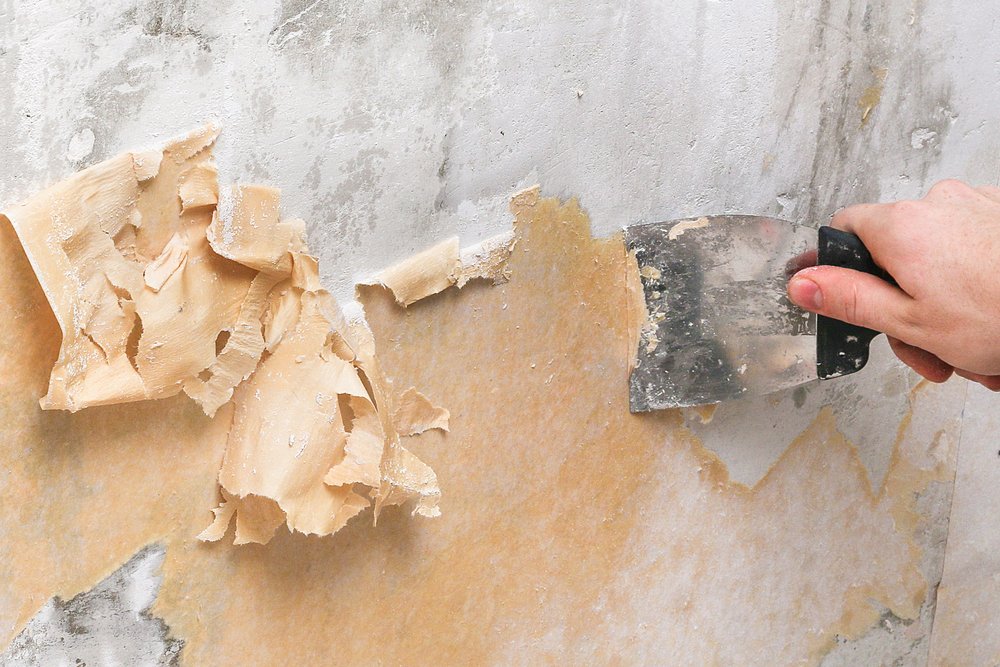 Hand die behang voorzichtig losmaakt van de muur met een behangafsteker.