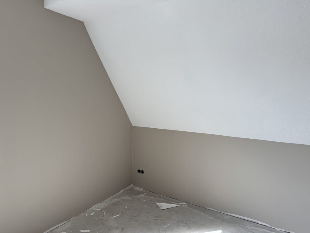 Zolderkamer met een schuine wand en kale wanden, de vloer afgedekt met folie