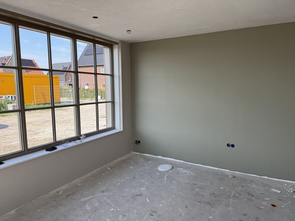 Kamer met een egaal afgewerkte grijsgroene wand en een groot raam