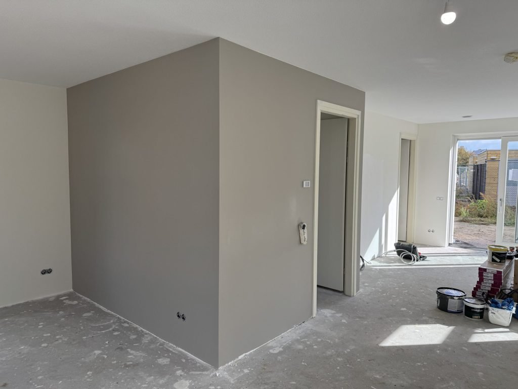 Gesausde grijze wand in een woning die wordt afgewerkt, met verfemmers op de vloer