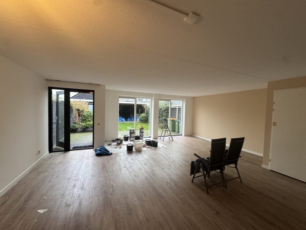 Ruime woonkamer met lichte wanden, een houten vloer en tuindeuren