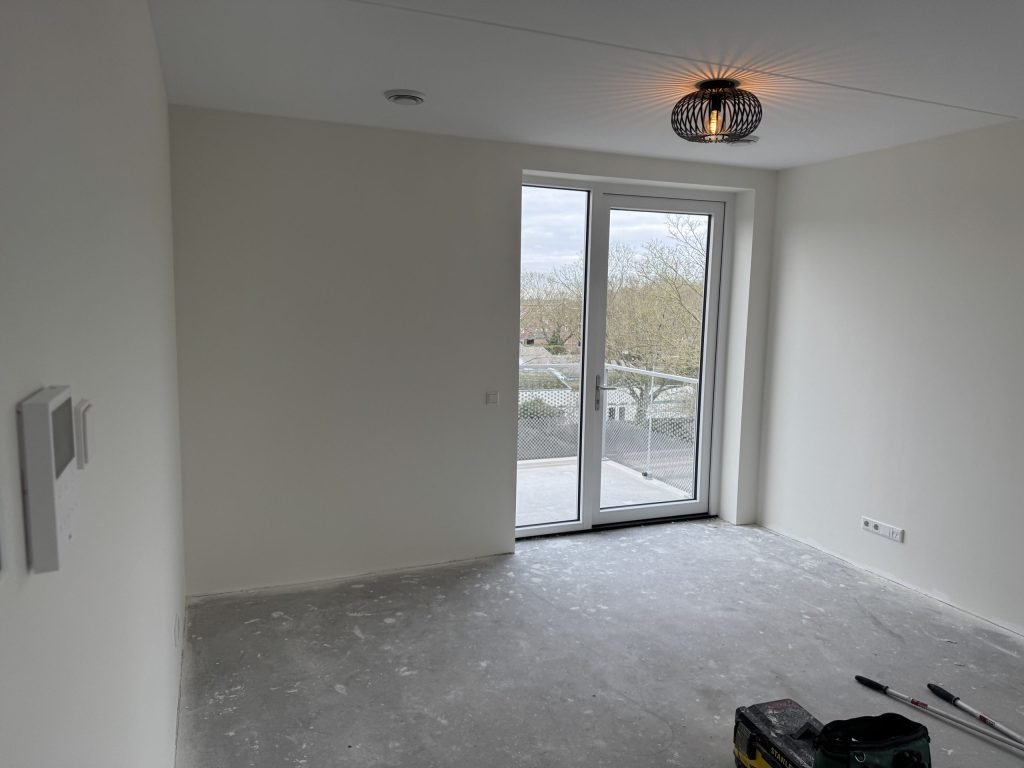 Lege kamer met kale wanden en een glazen deur naar het balkon