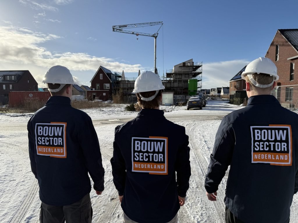Drie vakmensen van Bouwsector Nederland met witte helm op een besneeuwde bouwplaats met een kraan